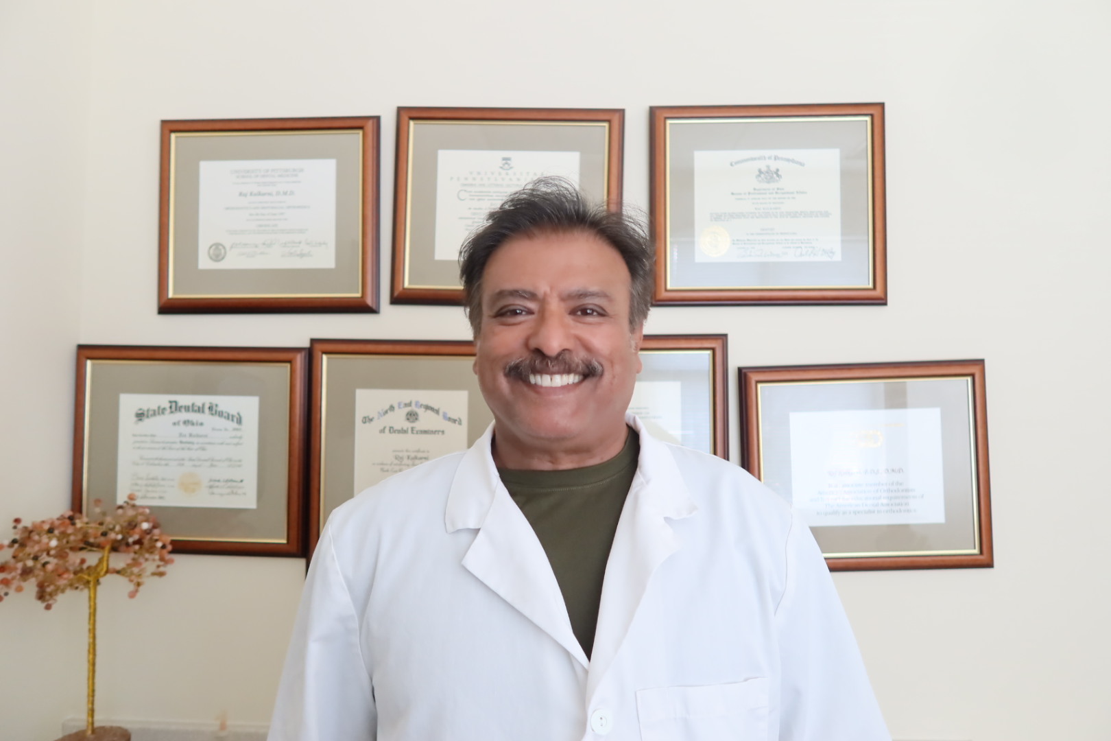 Dr. Raj Kulkarni in front of his diplomas and certificates at Kulkarni Orthodontics